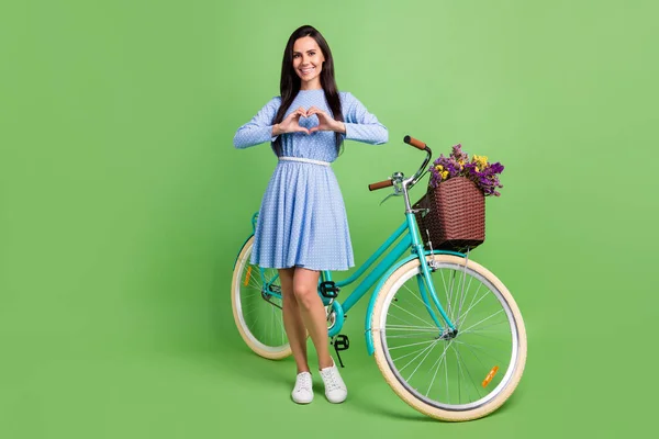 Foto de corpo inteiro de flerte senhora de cabelo marrom mostrar coração com vestido de desgaste de bicicleta isolado no fundo verde — Fotografia de Stock