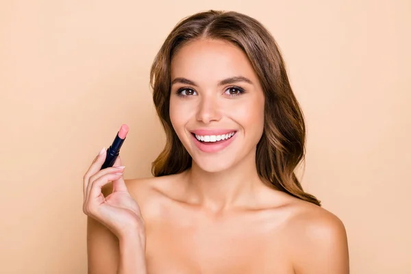 Photo of young happy positive smiling cheerful girl applying nude matte lipstick isolated on beige color background — Stock Photo, Image
