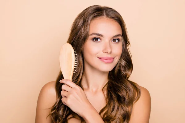 Photo of young beautiful lovely smiling girl brushing silky perfect brown wavy hair isolated on beige color background — Stock Photo, Image