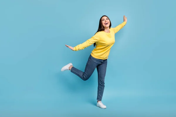 Foto van dromerige geïnspireerde dame dans vliegtuig pose look lege ruimte dragen gele trui jeans schoenen geïsoleerde blauwe achtergrond — Stockfoto