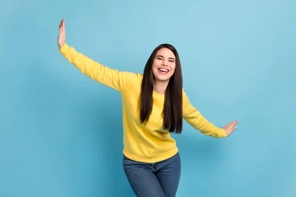 Foto di positivo adorabile signora danza aeroplano posa usura giallo ponticello jeans isolato blu sfondo — Foto Stock