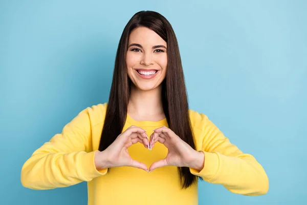 Retrato de bom otimista morena longo penteado senhora mostrar coração desgaste amarelo camisa isolado no brilhante azul cor fundo — Fotografia de Stock