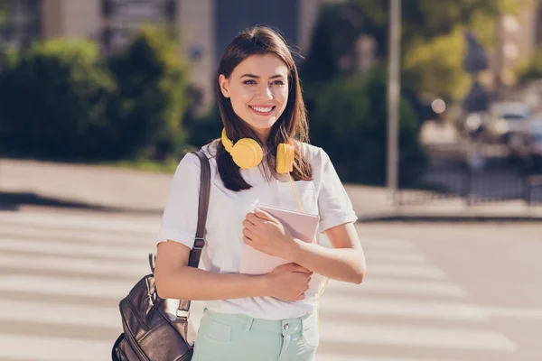 Foto retrato de menina mantendo livro vestindo mochila fones de ouvido amarelos sorrindo indo para a faculdade — Fotografia de Stock