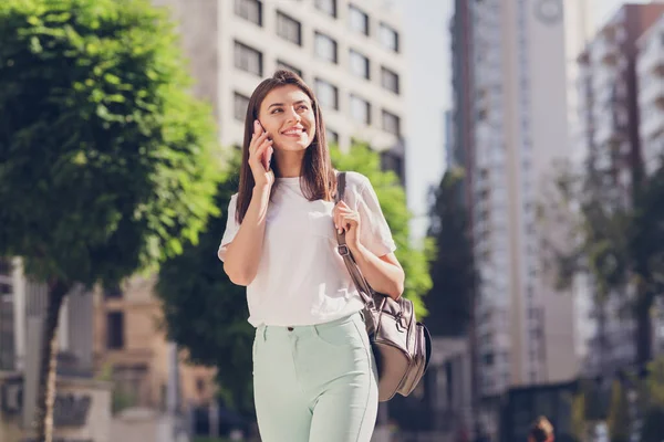 Фото оптимистичной брюнетки леди говорить по телефону носить белый мешок ткани прогуливаясь в парке снаружи — стоковое фото