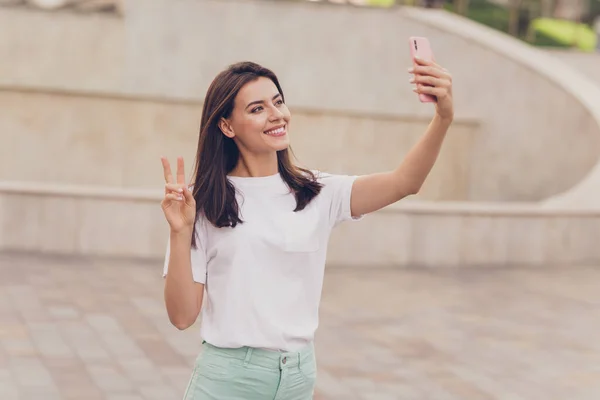 Foto de otimista morena senhora do selfie show v-sign desgaste branco t-shirt andando no parque fora — Fotografia de Stock