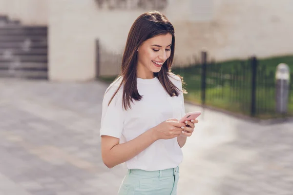 Profiel foto van optimistische brunette dame kijken telefoon dragen witte t-shirt wandelen in park buiten — Stockfoto