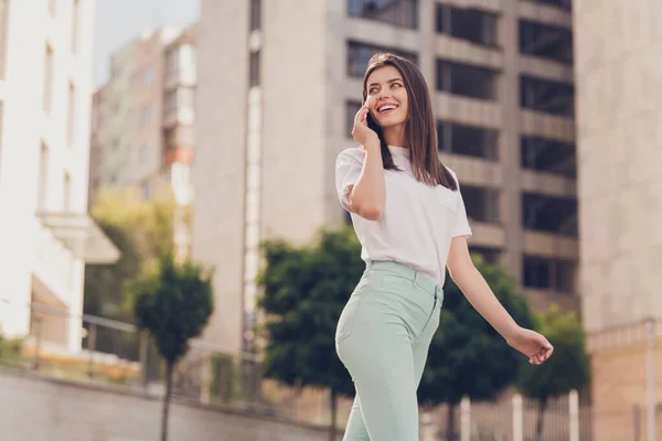Фотопортрет красивой девушки в белых брюках с бирюзовой футболкой, разговаривающей по мобильному телефону, гуляющей по летним улицам, радостно улыбающейся — стоковое фото