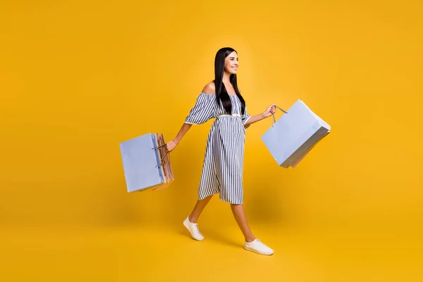 Plná délka fotografie rozkošné ženy oblečené off-ramena šaty chůze držení nákupních tašek izolované žluté barvy pozadí — Stock fotografie
