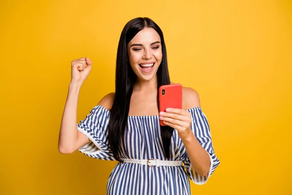 Foto de funky sorte jovem senhora usar vestido listrado olhando dispositivo moderno levantando punho isolado cor amarela fundo — Fotografia de Stock