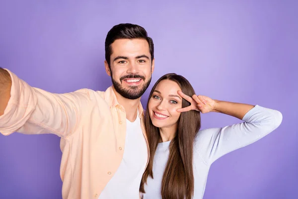Фото веселих брюнетки чоловік і жінка роблять v-знак коханців селфі ізольовані на фіолетовому кольоровому фоні — стокове фото