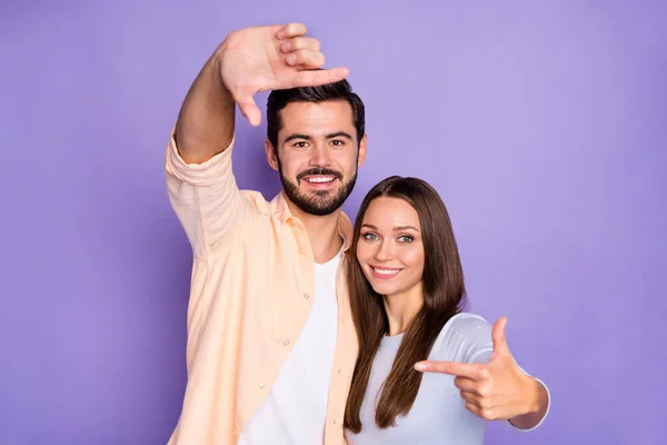 Foto de feliz criativo na moda casal morena mostrar câmera quadro dedos isolados no fundo cor roxa — Fotografia de Stock