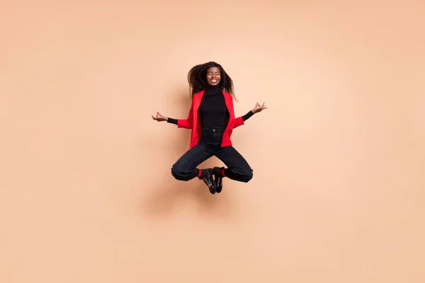 Foto de linda mujer concentrada de piel oscura rizada vestida chaqueta roja saltando chakras abiertos aislados color beige fondo — Foto de Stock