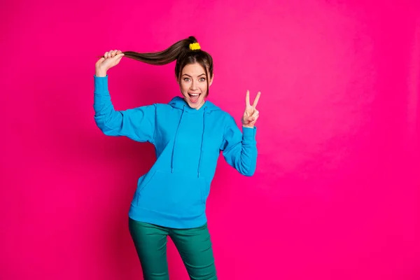 Foto de divertida chica alegre mano jugando mantenga el pelo abierto boca dedos muestran v-signo aislado en el fondo de color rosa — Foto de Stock