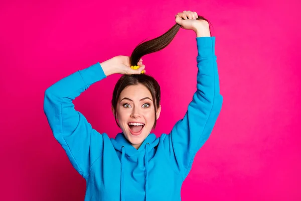 Fotografie ohromen veselá dáma otevřených úst paže držet hrát s vlasy ocas izolované na růžové barevné pozadí — Stock fotografie