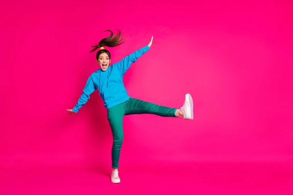 全长照片，滑稽而兴奋的年轻女士穿着蓝色毛衣跳舞，一条腿孤零零地站在明亮的粉红色背景下 — 图库照片