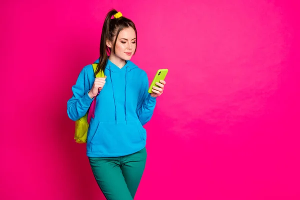Foto di carino dolce signora indossare blu maglione zaino chattare dispositivo moderno spazio vuoto isolato luminoso colore rosa sfondo — Foto Stock