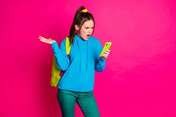 Φωτογραφία από δυστυχισμένη θυμωμένη γυναίκα ντυμένη μπλε hoodie σακίδιο αναζητούν gadget κενό χώρο απομονωμένο ζωντανό ροζ χρώμα φόντο — Φωτογραφία Αρχείου