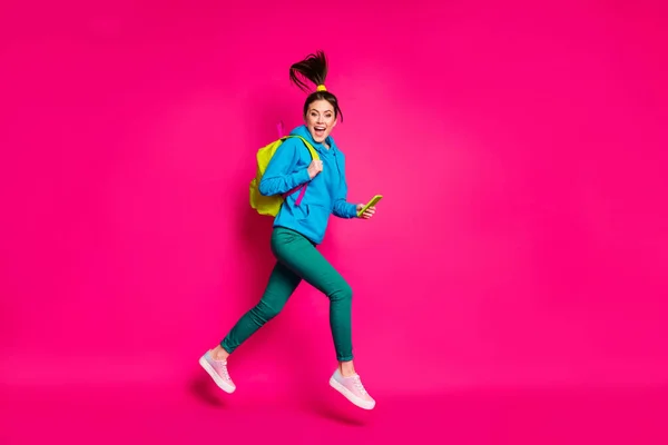 Foto de longitud completa de funky linda joven dama usar suéter azul mochila corriendo la celebración de dispositivo moderno aislado de color rosa fondo —  Fotos de Stock