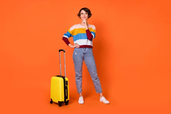 Полная длина портрет очаровательной леди стоять рядом с чемоданом руку на подбородок выглядят пустые места изолированы на оранжевом фоне цвета — стоковое фото