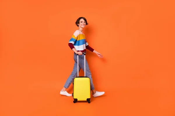 Ganzkörperprofil Porträt der charmanten Person Hand tragen Koffer zu Fuß Look Kamera isoliert auf orangefarbenem Hintergrund — Stockfoto