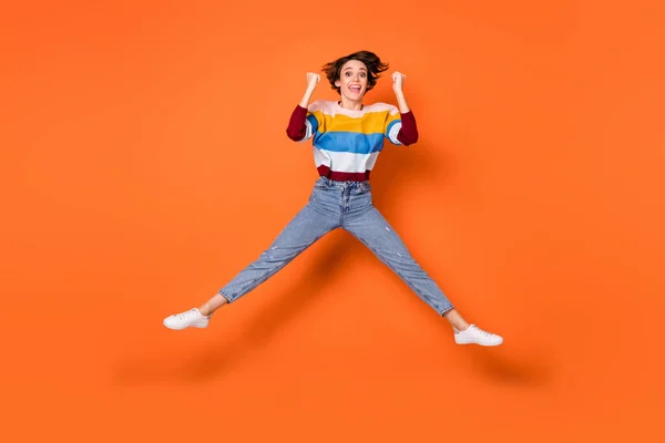 Full size photo of astonished lady jumping high fists up celebrate triumph isolated on orange color background — Stock Photo, Image