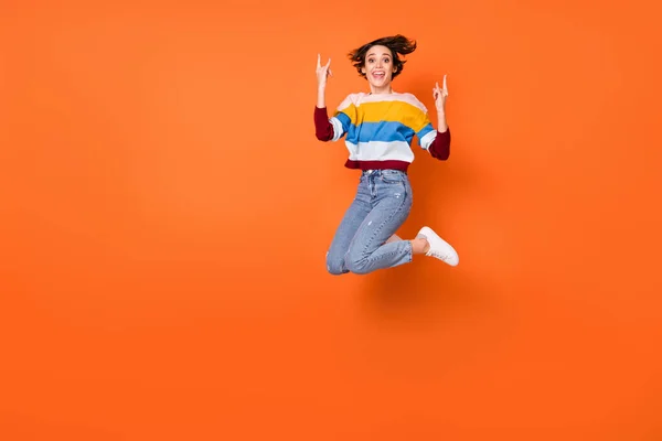 Foto von süßen harten jungen Frau tragen gestreiften Pullover Springen zeigt Hard Rock Zeichen isoliert orange Farbe Hintergrund — Stockfoto