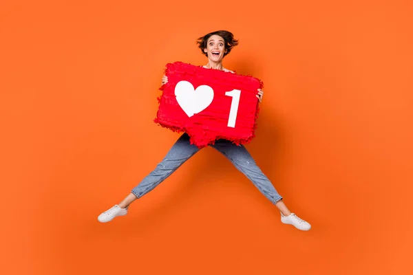 Foto de brillante divertida joven dama vestida a rayas suéter saltando alto celebración grande como botón aislado color naranja fondo —  Fotos de Stock