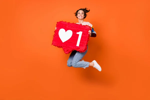 Foto de linda dulce mujer joven usar suéter a rayas saltando sosteniendo rojo como signo aislado color naranja fondo —  Fotos de Stock