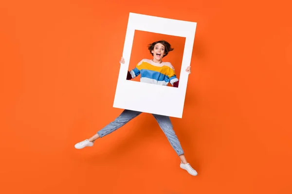 Plná velikost fotografie užaslé dívky skákání ruce držet rám otevřená ústa izolované na oranžové barvy pozadí — Stock fotografie