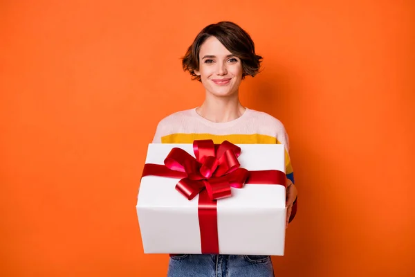 Фото очаровательной девушки руки держать giftbox улыбка смотреть камеру носить свитер изолирован на оранжевом фоне цвета — стоковое фото