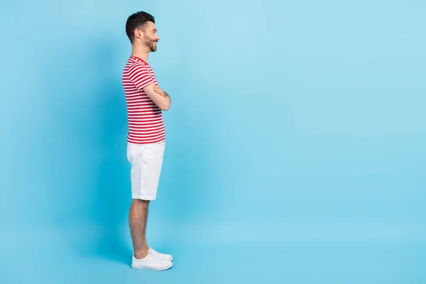 Profilo a figura intera lato foto di affascinante uomo sguardo vuoto spazio tenere le mani incrociate isolato su sfondo di colore blu — Foto Stock