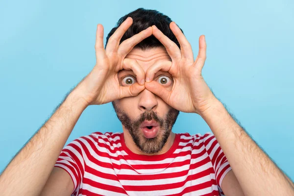 Foto de divertido chocado joven desgaste rojo mostrando gafas dedos cubren ojos aislados color azul fondo —  Fotos de Stock