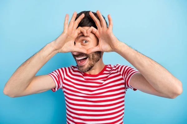 Foto de un joven bastante positivo vestido con una camiseta a rayas que muestra los dedos cubierta del corazón cara aislada de color azul de fondo — Foto de Stock
