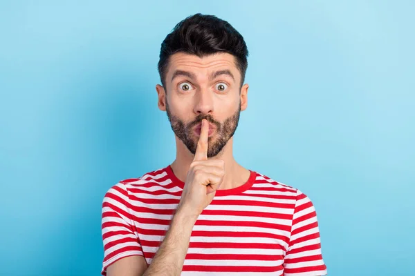 Photo de jeune homme assez impressionné habillé rayé t-shirt doigt lèvres demander de ne pas dire secrets isolé fond de couleur bleue — Photo