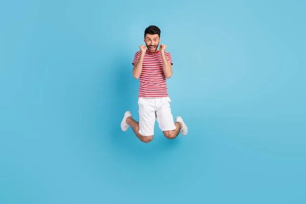 Foto de comprimento total de funky sorte jovem vestido listrado t-shirt saltando altos punhos em ascensão isolado azul cor fundo — Fotografia de Stock