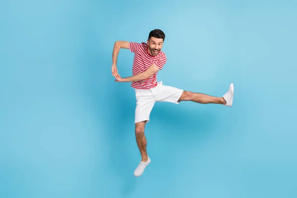 Pełna długość zdjęcie pozytywne śmieszne młody człowiek ubrany w paski t-shirt skoki wysoki taniec odizolowany niebieski kolor tło — Zdjęcie stockowe