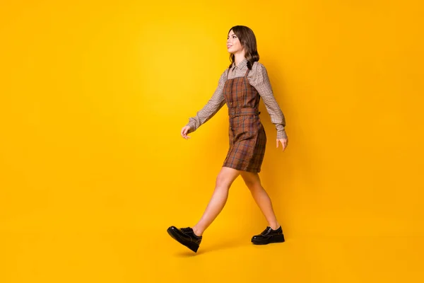Full size profiel foto van optimistische brunette dame ga dragen bruin shirt jurk laarzen geïsoleerd op levendige gele achtergrond — Stockfoto
