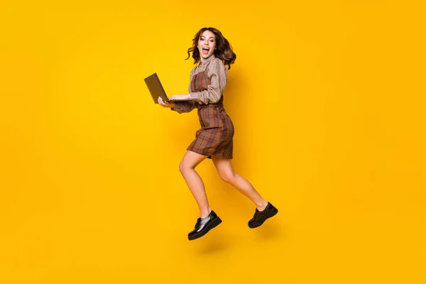 Full size profile photo of optimistic brunette lady with laptop jump wear shirt dress sneakers isolated on vivid yellow background — Stock Photo, Image