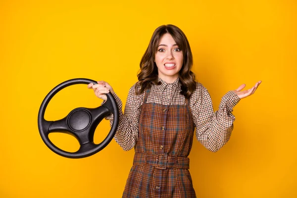 Фотопортрет девушки не знает, как управлять, сохраняя руль изолированным на ярком желтом фоне — стоковое фото