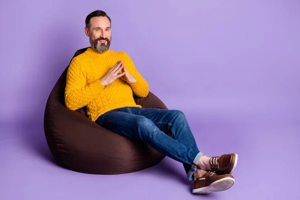 Foto de hombre sit beanbag sostener los dedos sonrisa dentada usar suéter amarillo jeans calzado aislado fondo violeta —  Fotos de Stock