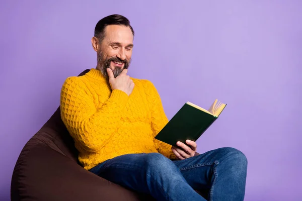 Foto de hombre sit beanbag hold book leer dedo barbilla desgaste amarillo jersey jeans aislado fondo púrpura — Foto de Stock