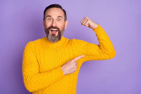 Фото взволнованного сильного мужчины поднять руку прямой палец показать бицепсы носить желтый пуловер изолированный фиолетовый фон — стоковое фото
