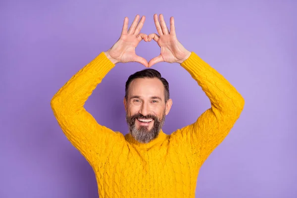 Fénykép a romantikus szakállas férfi emelje fel a kezét mutatják szív figura kopás sárga pulóver elszigetelt ibolya háttér — Stock Fotó