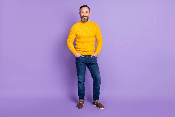Bild av skäggig man händer fickor ser kamera bära gul pullover jeans skor isolerad violett bakgrund — Stockfoto