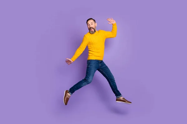 Photo of excited man jump run raise hands wear yellow pullover jeans footwear isolated violet background — Stock Photo, Image