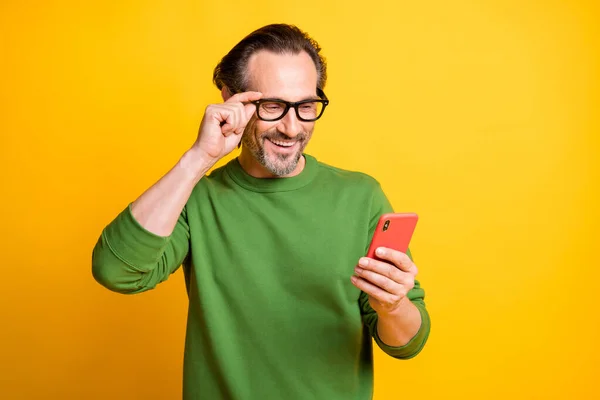 ハンサムな男の写真携帯電話のルック画面調整仕様は、緑のプルオーバー孤立黄色の背景を着用 — ストック写真