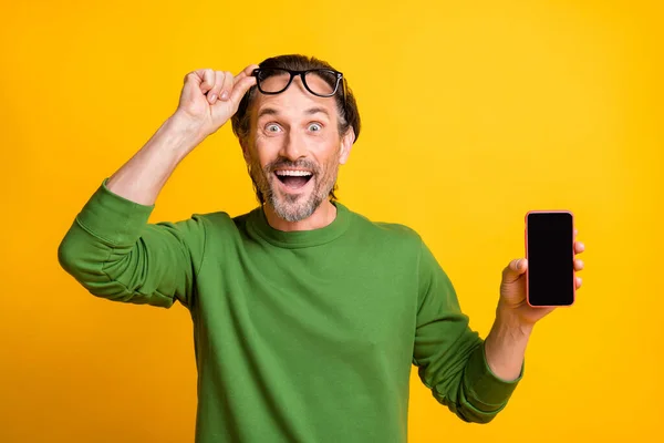 Foto de chico despegar especificaciones que muestran la pantalla del teléfono espacio vacío desgaste gafas verde jersey aislado color amarillo fondo — Foto de Stock