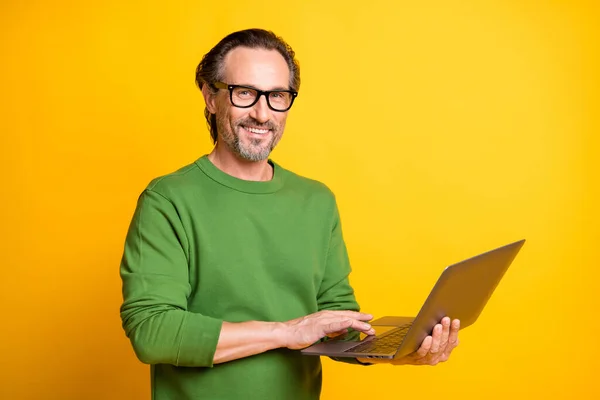 Bild av man hålla netbook hand touch pad bära glasögon grön tröja isolerad gul färg bakgrund — Stockfoto