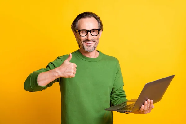 Foto van man houden computer verhogen duim omhoog tand glimlach dragen brillen groen trui geïsoleerde gele kleur achtergrond — Stockfoto