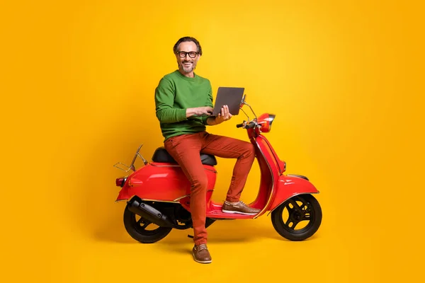 Erkek fotoğrafında, dizüstü bilgisayarda scooter kullanırken gözlüklü, yeşil kazaklı ayakkabılı, izole sarı arka plan. — Stok fotoğraf